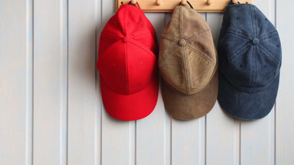 Three baseball caps, red, tan corduroy and faded navy, hanging on a wooden peg rail