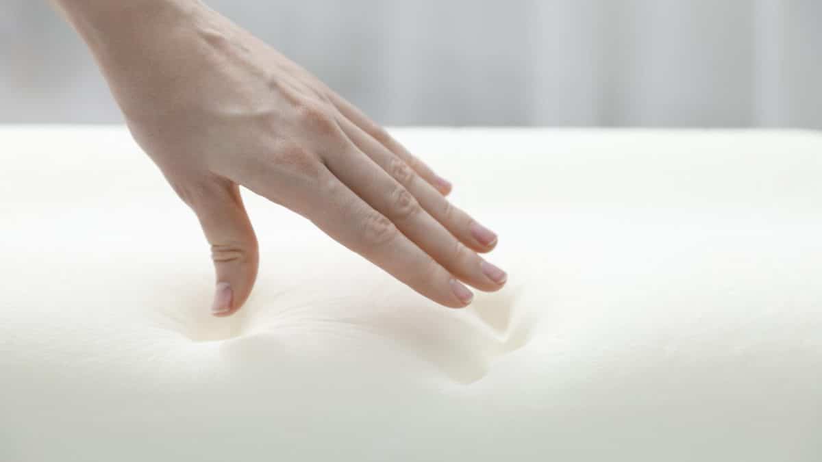 A hand pressing into white memory foam, leaving finger dents that refill slowly