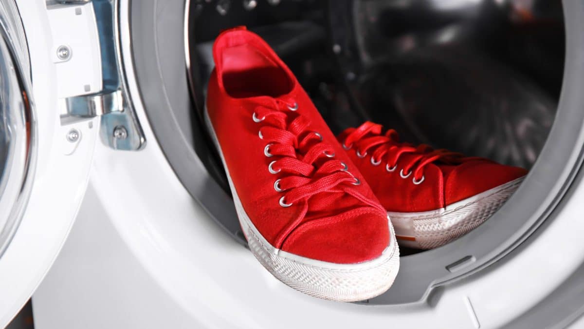 Red canvas sneakers resting on the open door of a front-loading washing machine