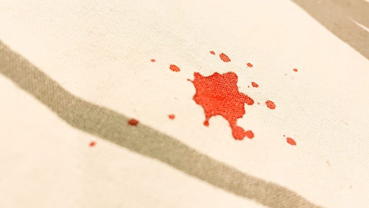 Close-up of a single red blood drop absorbed into a woven cream cotton cloth