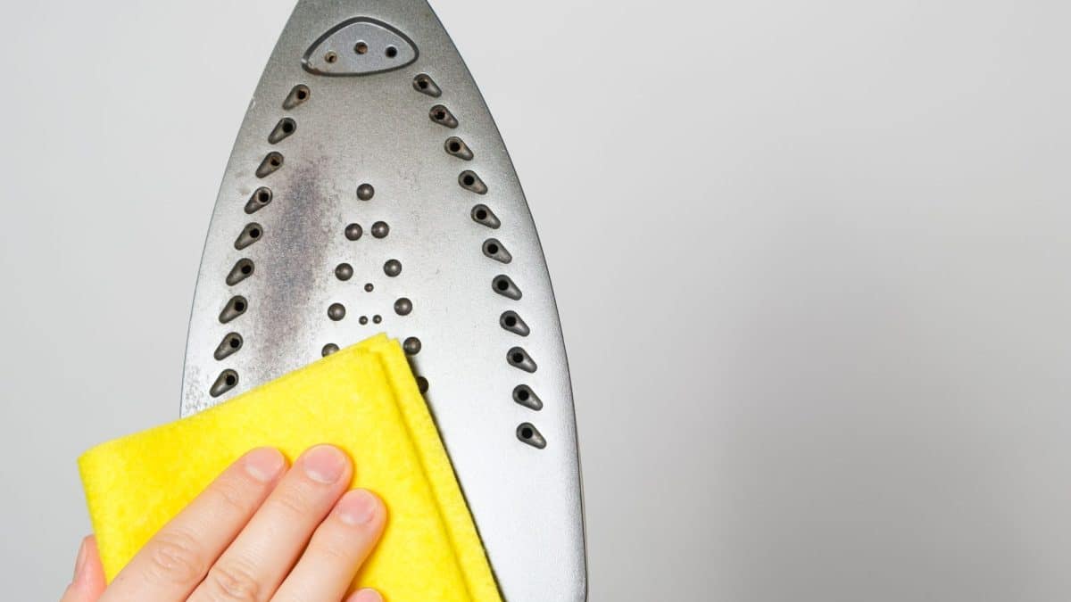A hand wiping the metal soleplate of an iron with a folded yellow cloth