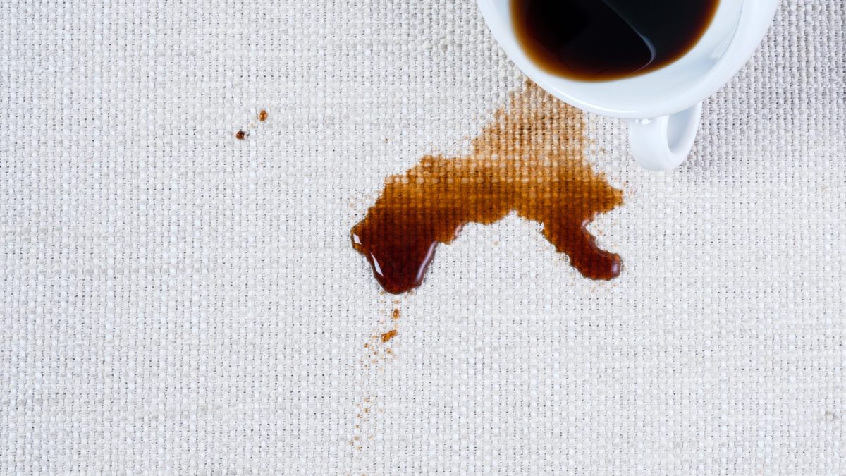 Black coffee spilled from a white cup soaking into a woven linen cloth