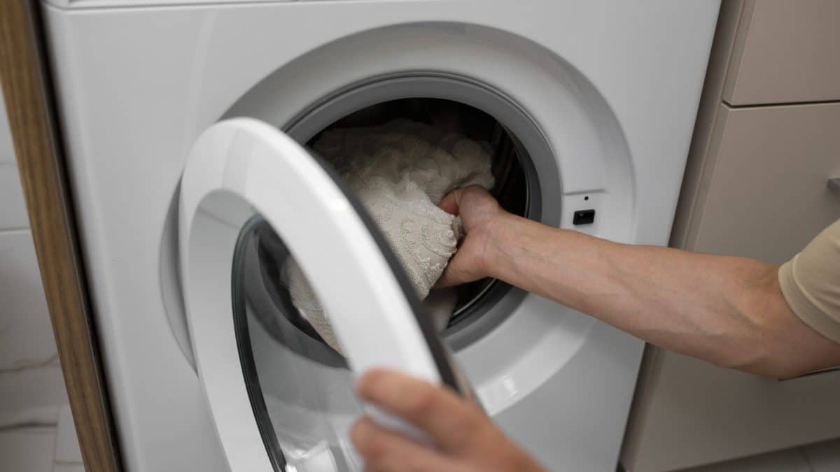 Arm pushing a bulky pale comforter into the drum of a front-loading washing machine