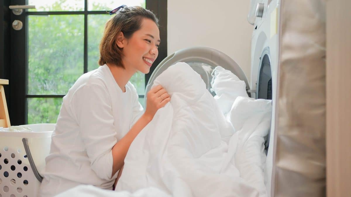 Woman feeding a bulky white comforter into the drum of a front-loading washing machine