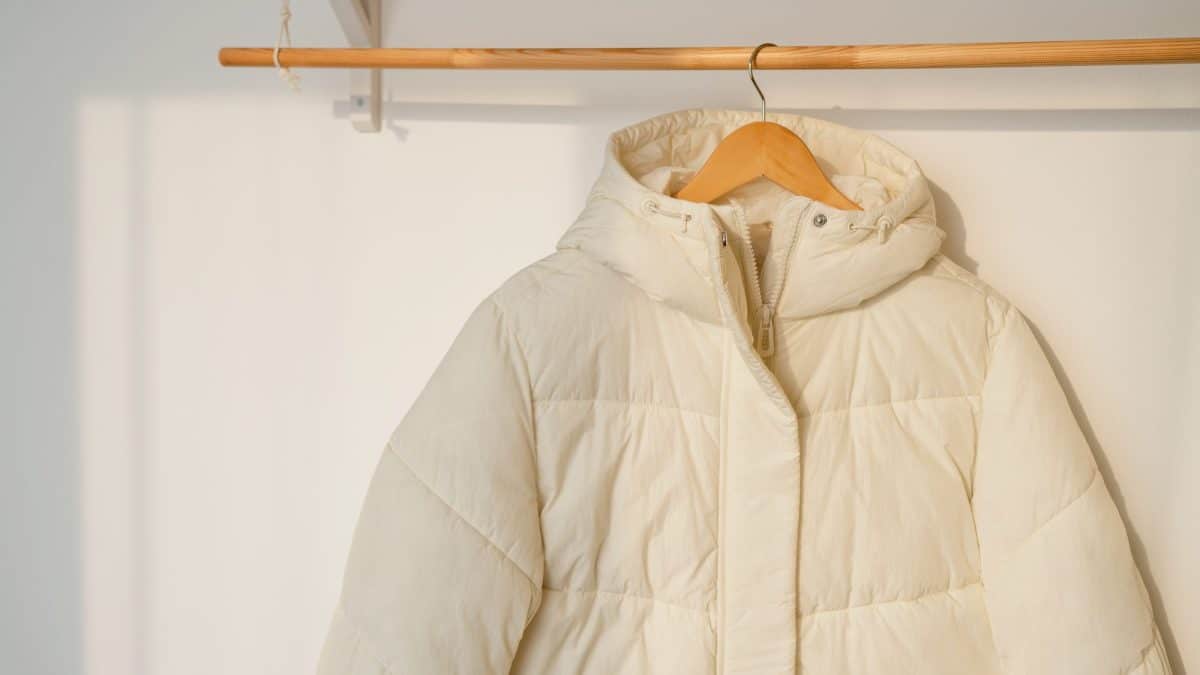 Cream hooded puffer jacket on a wooden hanger from a closet rail indoors