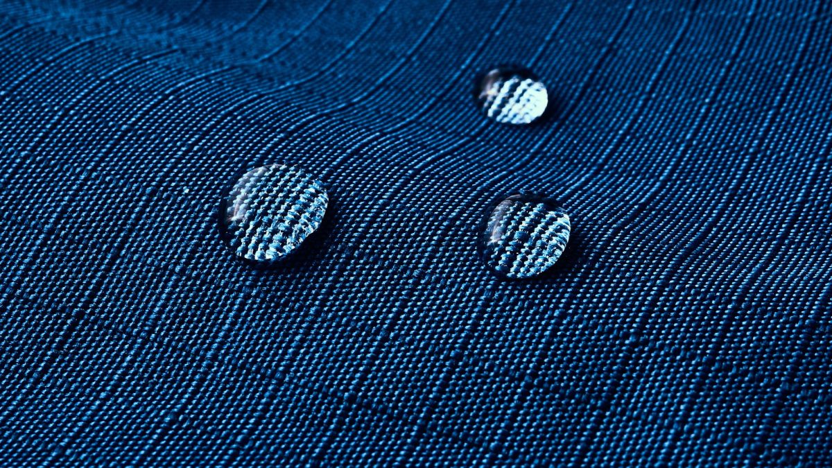 Three water droplets sitting on the weave of dark blue ripstop jacket fabric