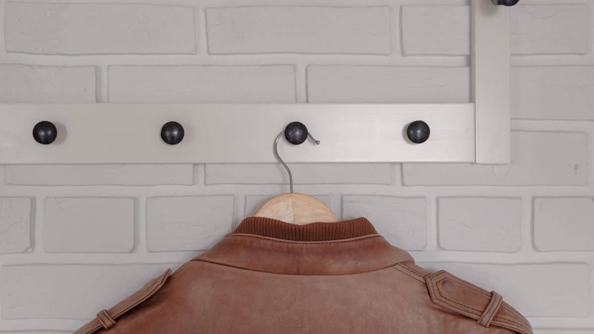 Brown leather jacket on a wooden hanger hung from a white peg rail indoors