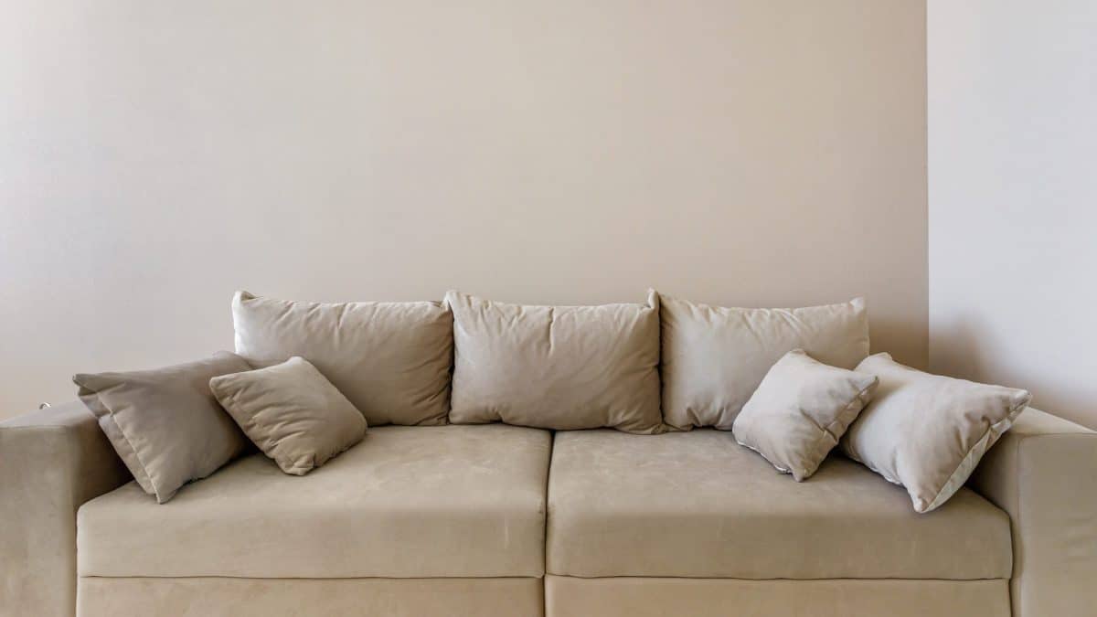 Beige microsuede sofa with matching cushions standing against a plain wall in a living room