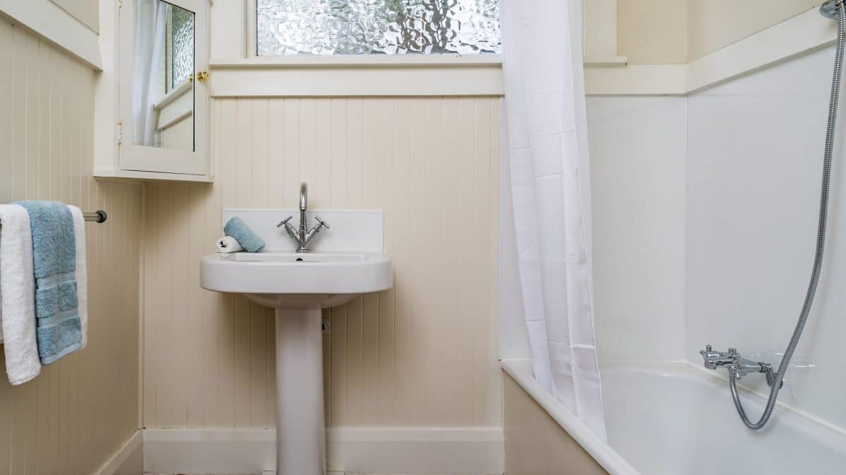 White shower curtain hanging beside a bathtub in a small daylit apartment bathroom