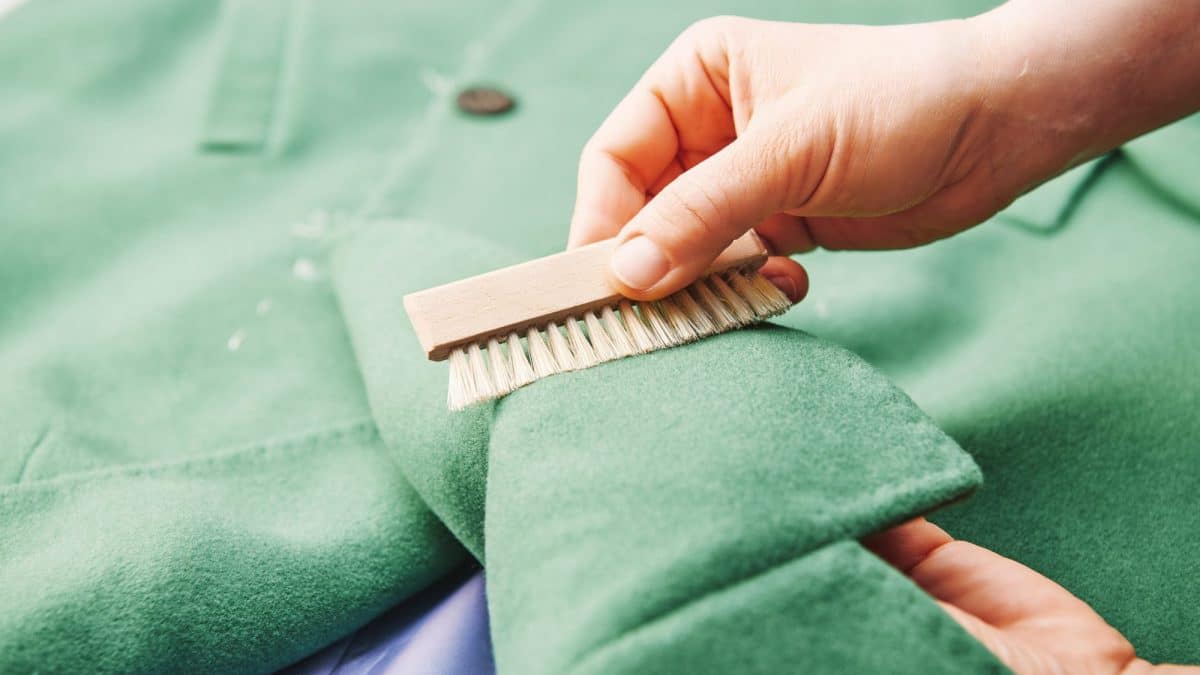 A wooden-handled garment brush worked along the nap of a green suede coat