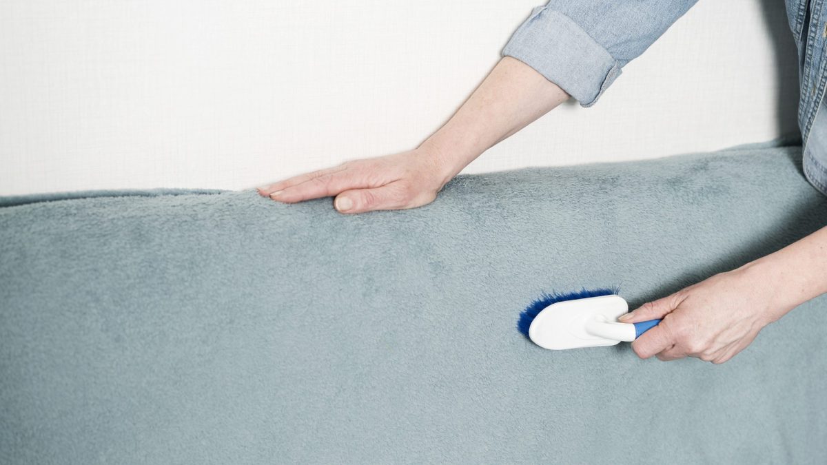Hand steadying a sofa back while brushing the napped upholstery with a soft-bristled brush