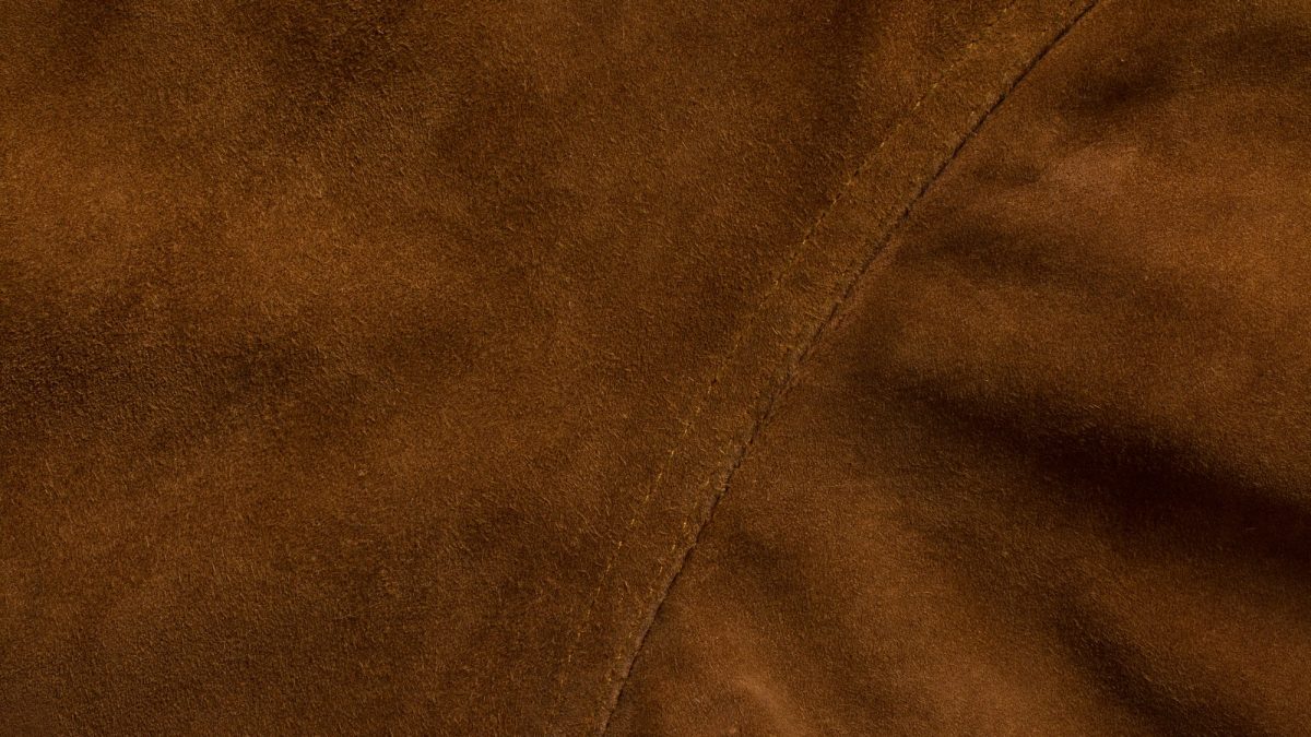 Close-up of brown suede jacket panels meeting along a stitched seam, nap catching the light