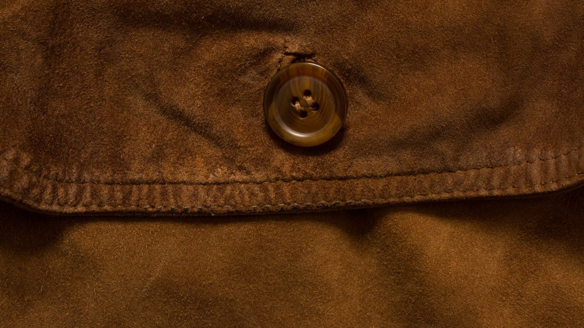 Close-up of a brown suede jacket pocket flap, seam stitching and horn button