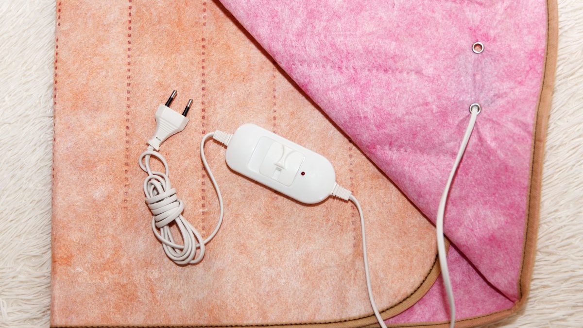 Electric blanket spread on a bed with its white controller and plug coiled on top