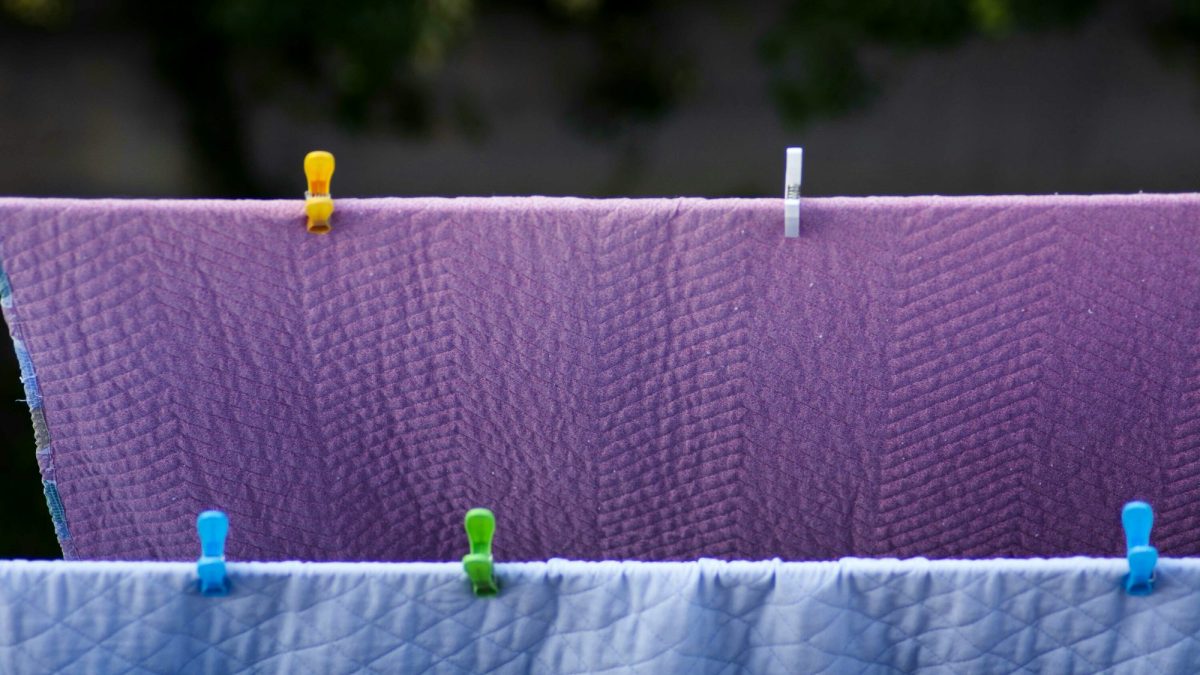 Two blankets hanging over an outdoor clothesline, held with coloured pegs, drying in daylight