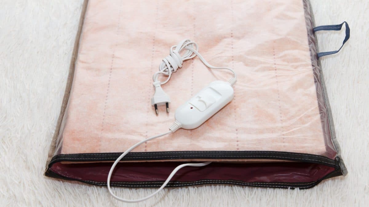 Electric blanket folded flat with its detachable controller and power lead lying unplugged on top