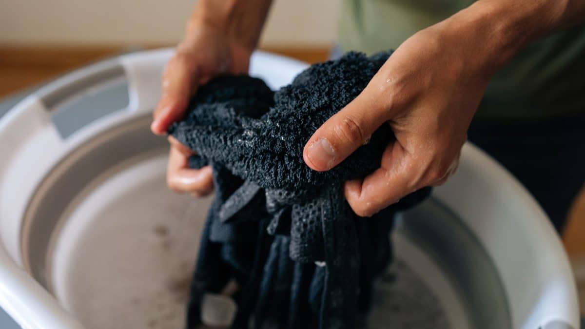 Two hands lifting a dark knitted garment out of a basin of soapy water