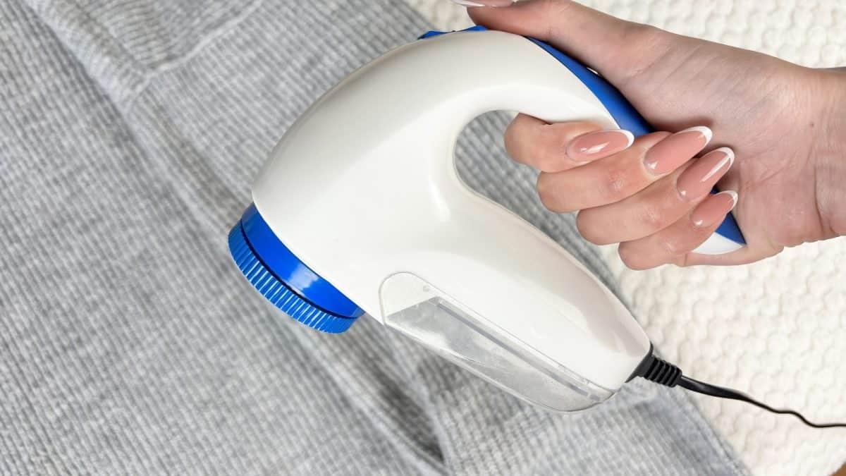 A hand running an electric fabric shaver across the surface of a grey knit sweater