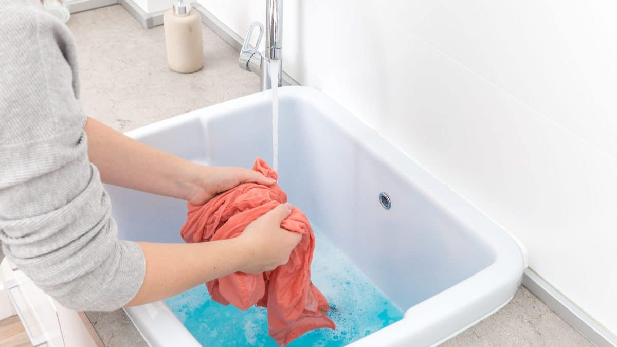 Woman washing a red garment by hand in a white utility sink under running water