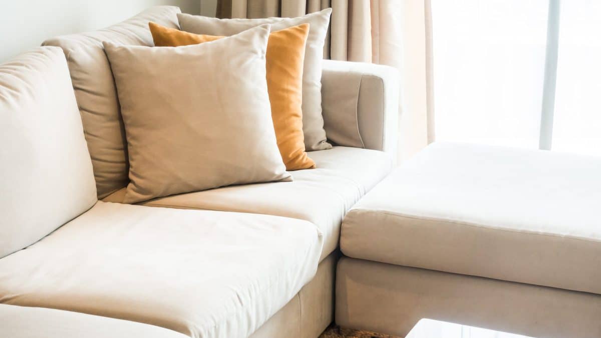 Cream fabric sectional couch with separate seat cushions and back cushions beside a bright window