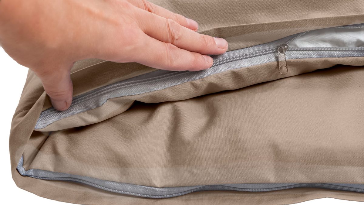 Hands sliding open the zipper along the edge of a tan cushion cover
