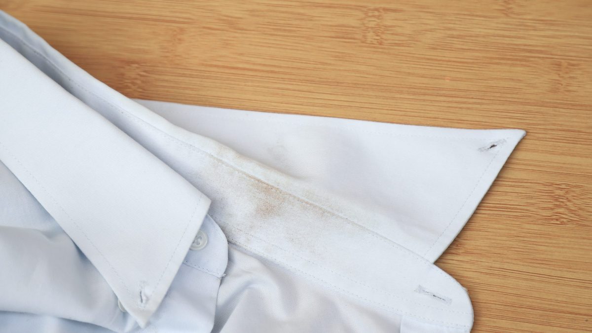 White cotton shirt spread on a wooden table with yellow-brown staining along the collar and shoulder seam