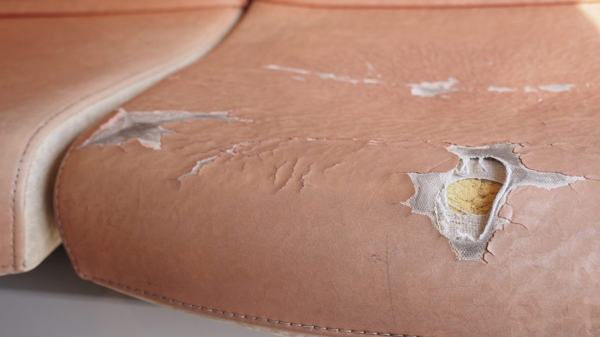 Pink faux leather seat with the coating flaked away, exposing pale woven backing and foam