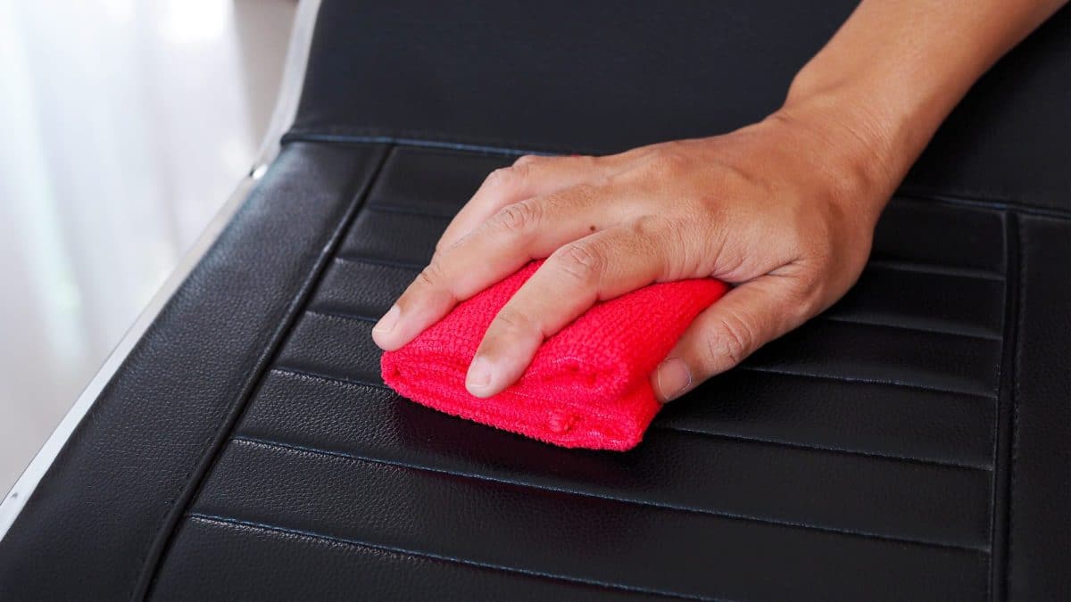 A bare hand pressing a folded red microfiber cloth across a black faux leather seat