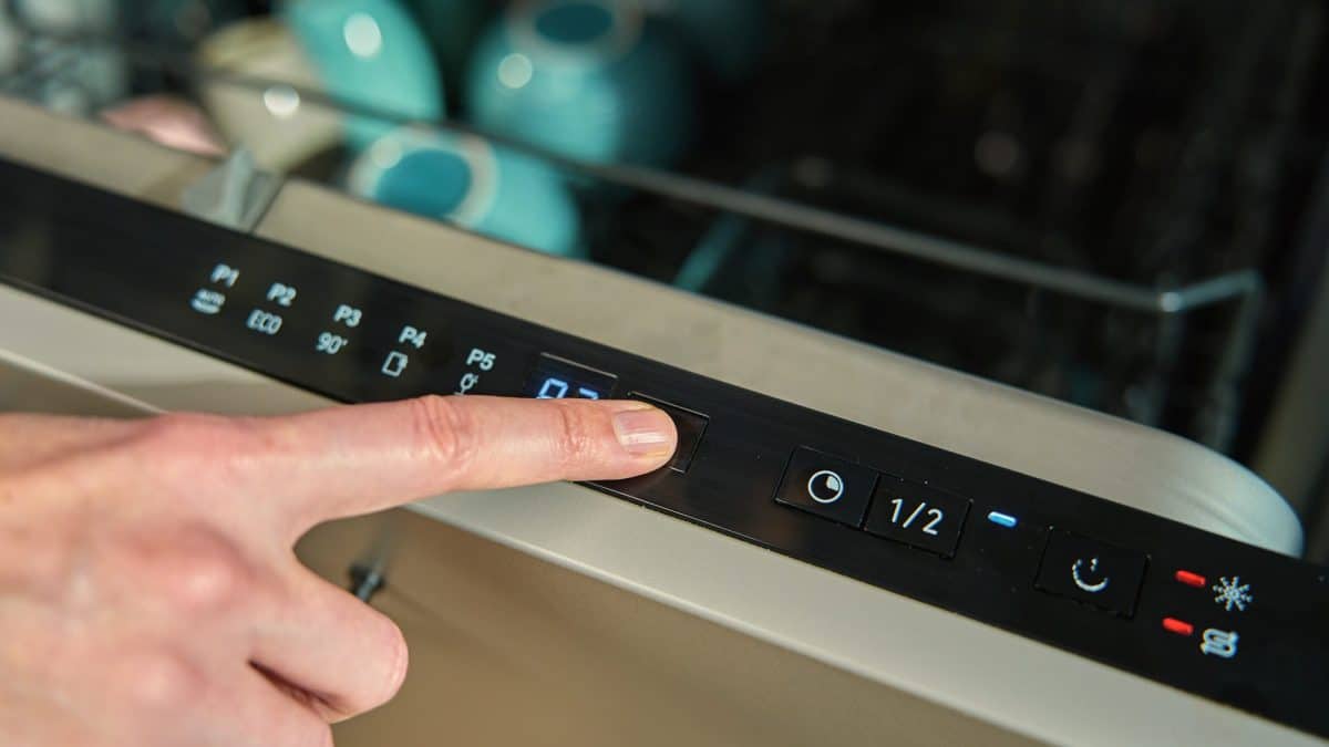 A finger pressing a cycle button on the control panel of an open dishwasher door
