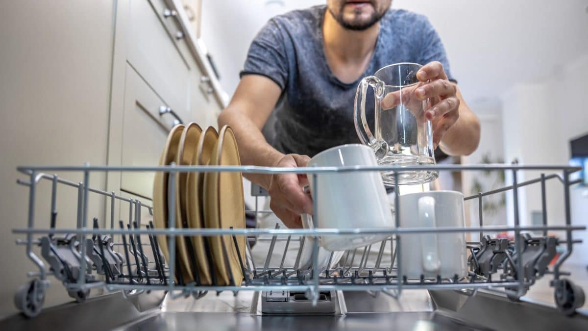 Hands placing a glass mug into the pulled-out rack of an open dishwasher