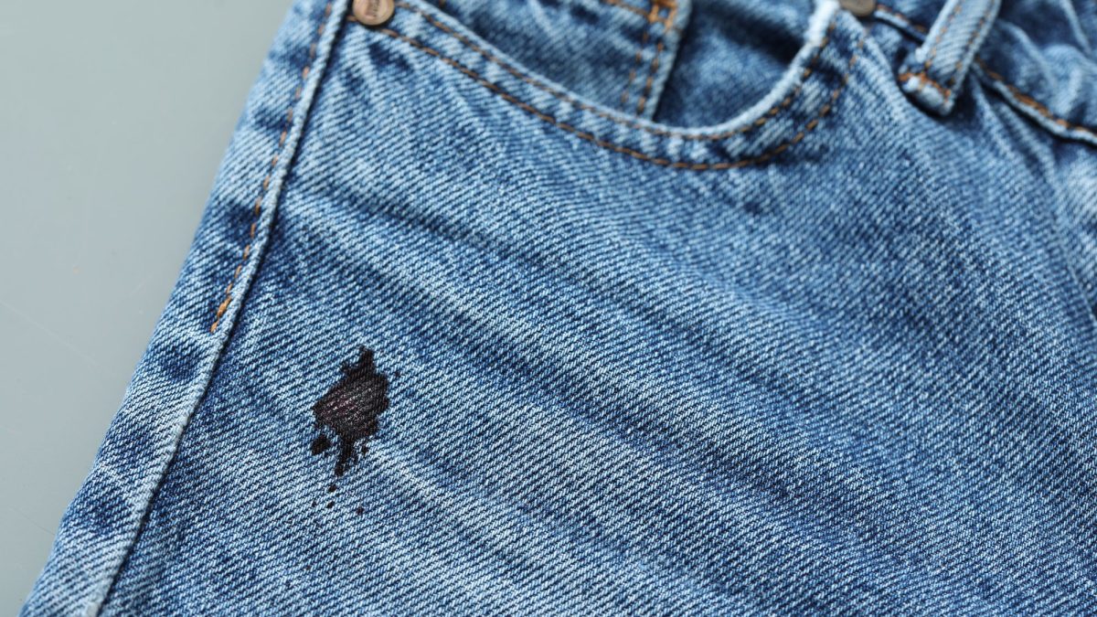 Close-up of a black ink blot with scattered specks soaked into blue denim jeans