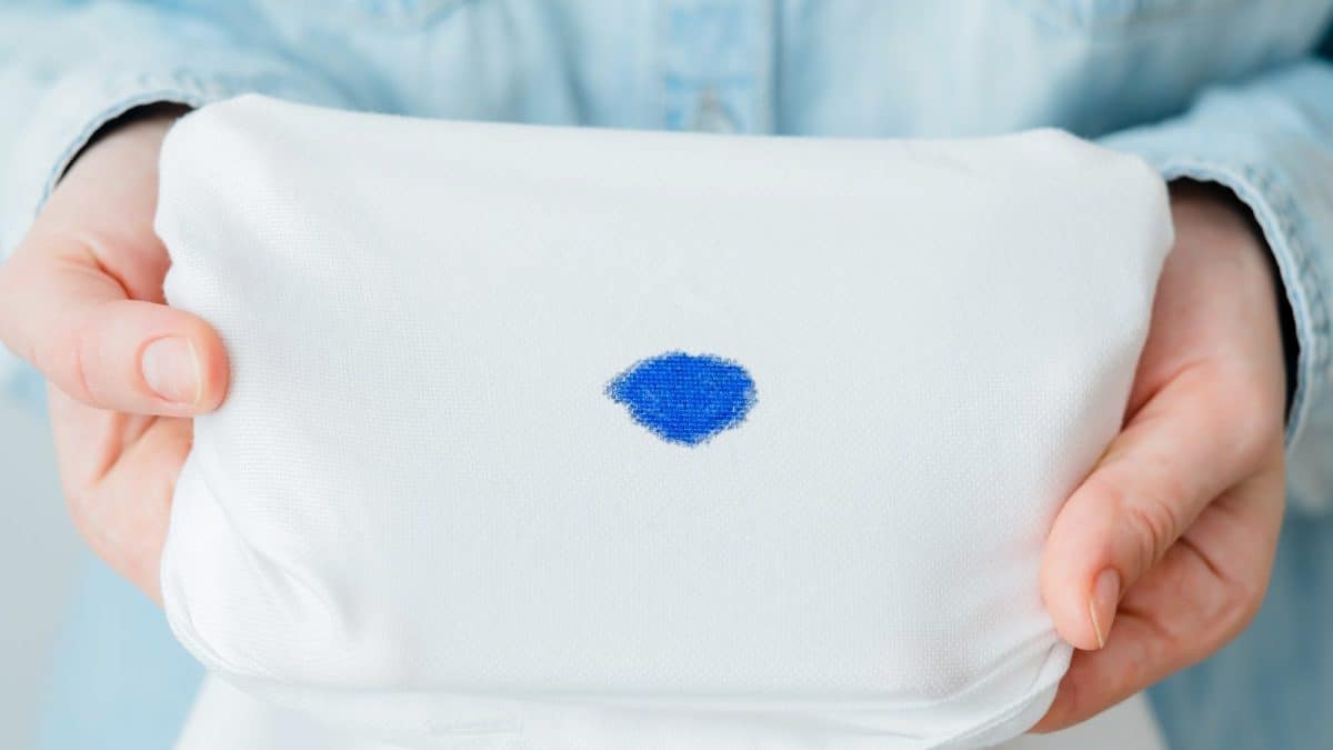 Two hands stretch a white garment flat around a solid blue ink stain