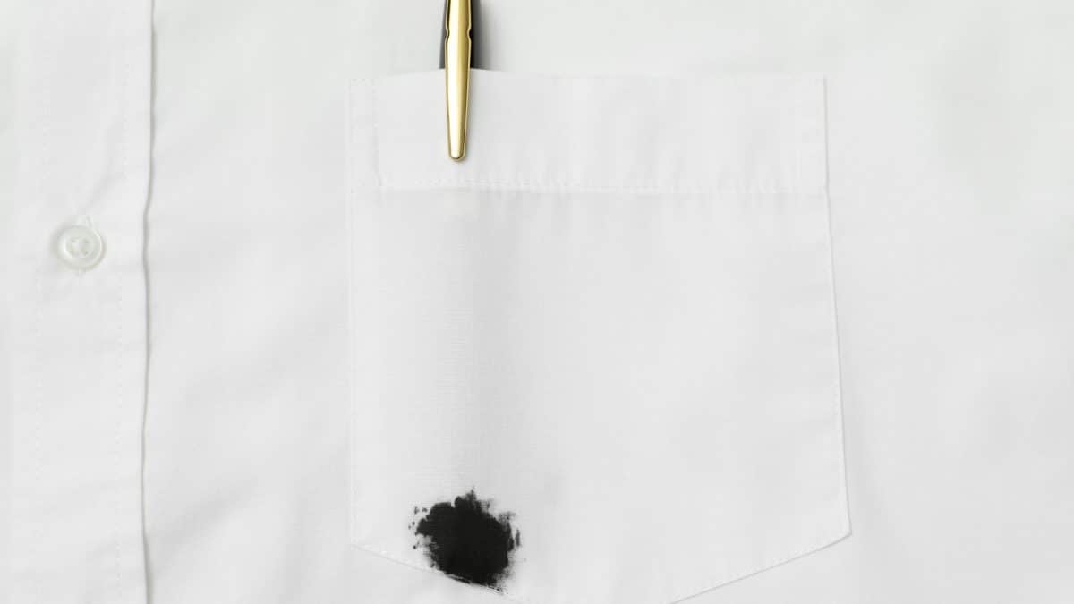 Black ink blot on a white shirt below the pocket, with a pen clipped above