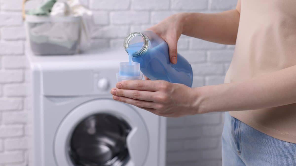 Hand pouring liquid fabric softener from a bottle into its measuring cap indoors