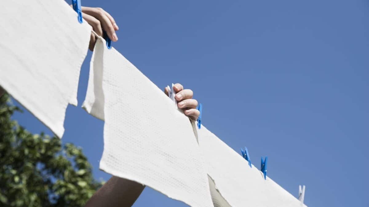 Hands pegging white laundry onto an outdoor line against a bright blue sky