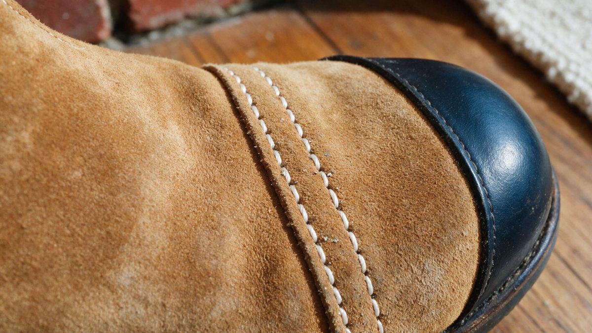 Macro close-up of a tan suede boot toe, where the suede vamp is stitched to a dark leather toe cap