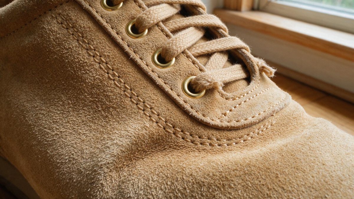 Close-up of a tan suede upper showing the raised nap, a stitched seam and flat laces