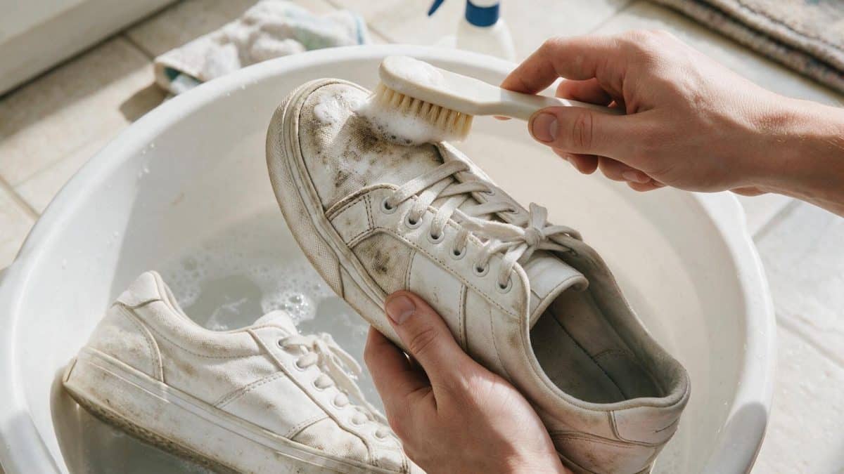 Hands scrubbing a dirt-marked white sneaker with a small brush over a basin